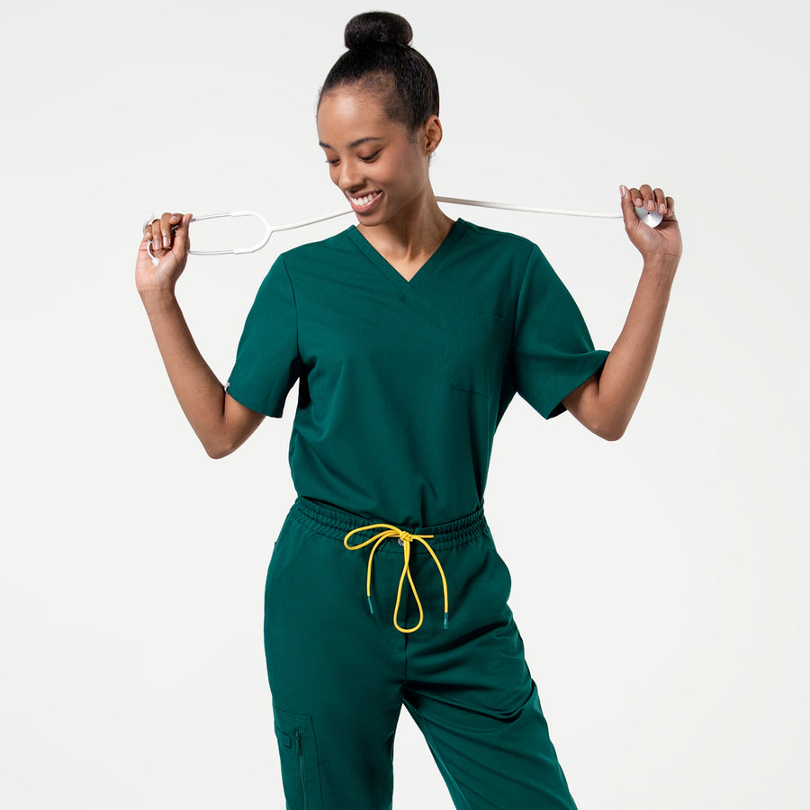 Model in the Women's Pine Green 3-Pocket Scrub Top, posing casually with a white stethoscope, upper body shot