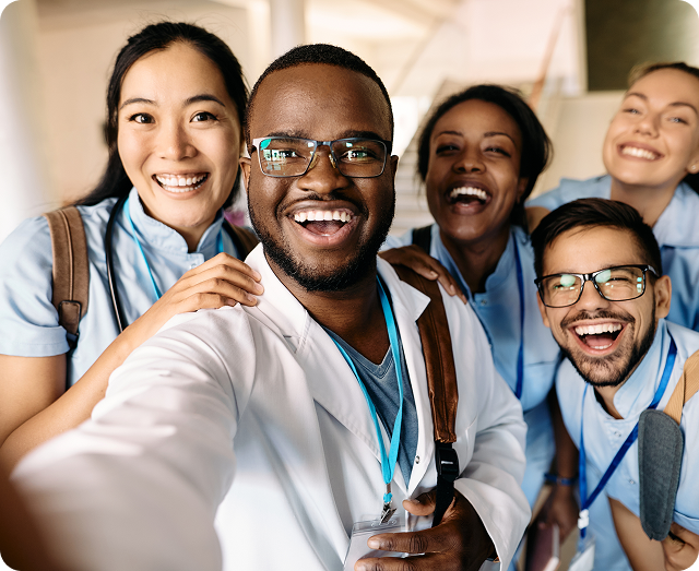 A group of medical students talking a selfie wearing light blue scrubs and lab coats.