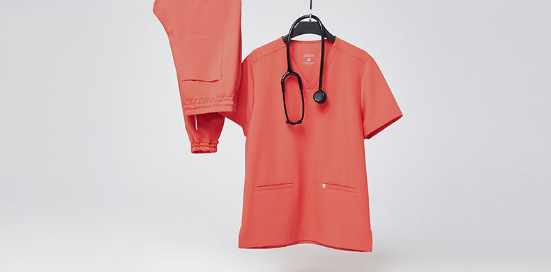 Zenir Tiger Orange Scrub top and bottom hanging in center frame on a black hanger, with a black stethoscope around the neckline.