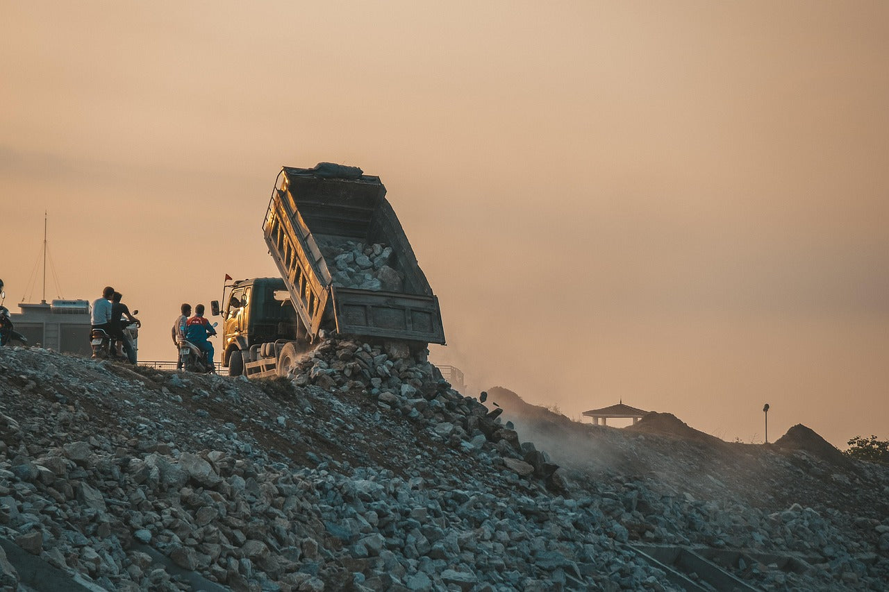 Image of Wasteland with trash on large hills, with a large trash truck dropping more garbage and people standing next to it.