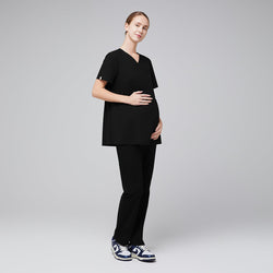 Image of Model wearing black maternity scrub top and matching scrub pants, with her hand holding her pregnancy bump.