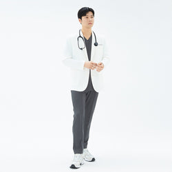 Image of Man standing with white background with a white lab coat and a charcoal gray set of scrubs under.