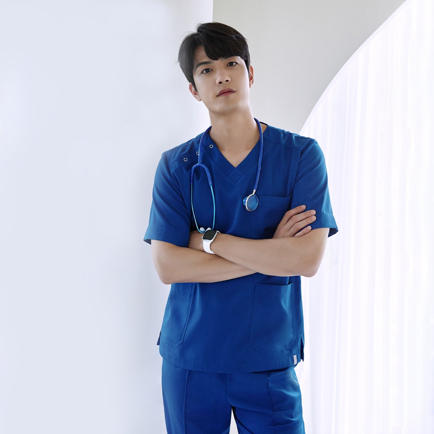 Image of Male model in a Royal Blue DS-167 scrub top standing with arms crossed and a stethoscope around his neck, highlighting the relaxed fit and chest pocket.