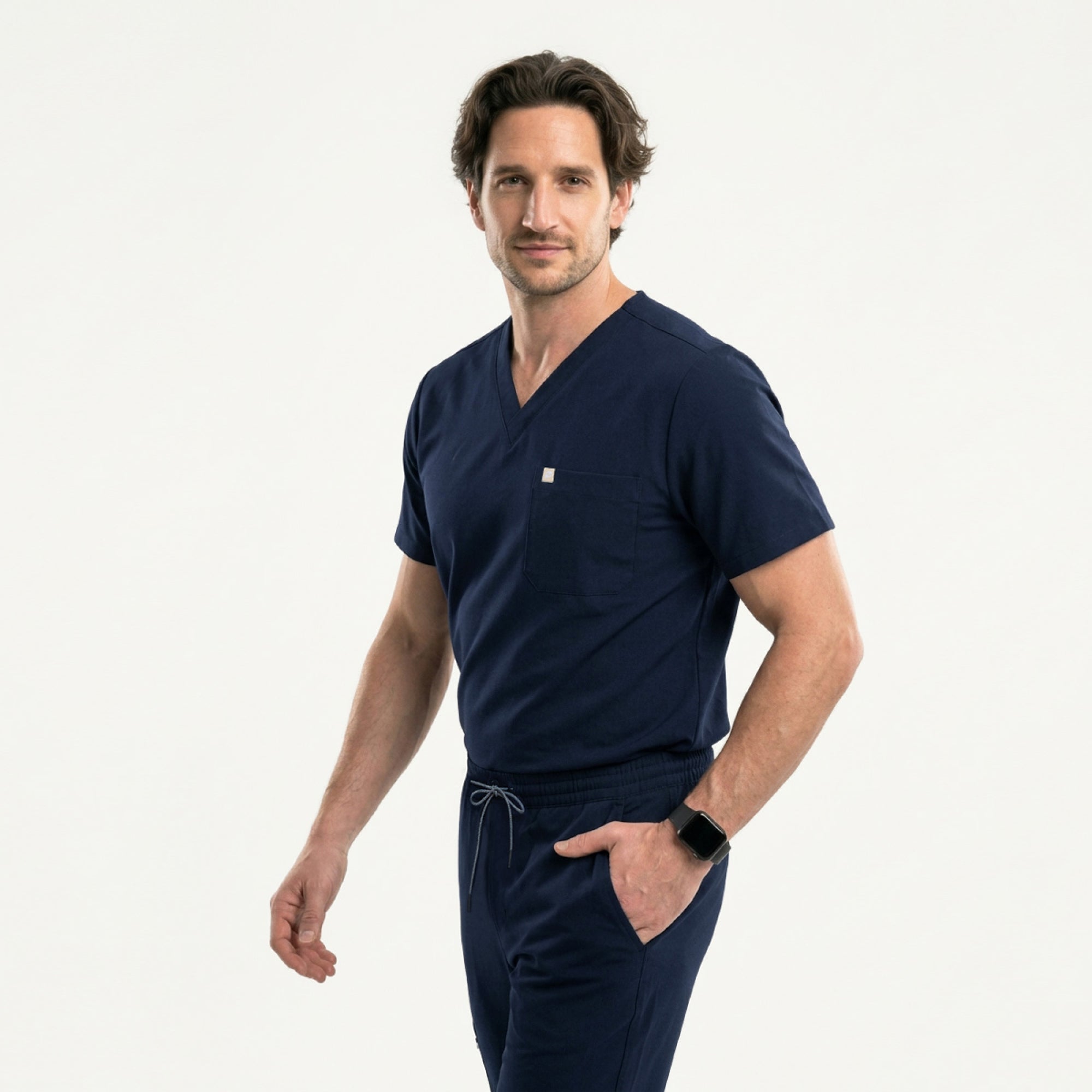 Image of With one hand in his pocket, the male model wears an Eco Navy scrub set and looks slightly to the side with a composed expression.