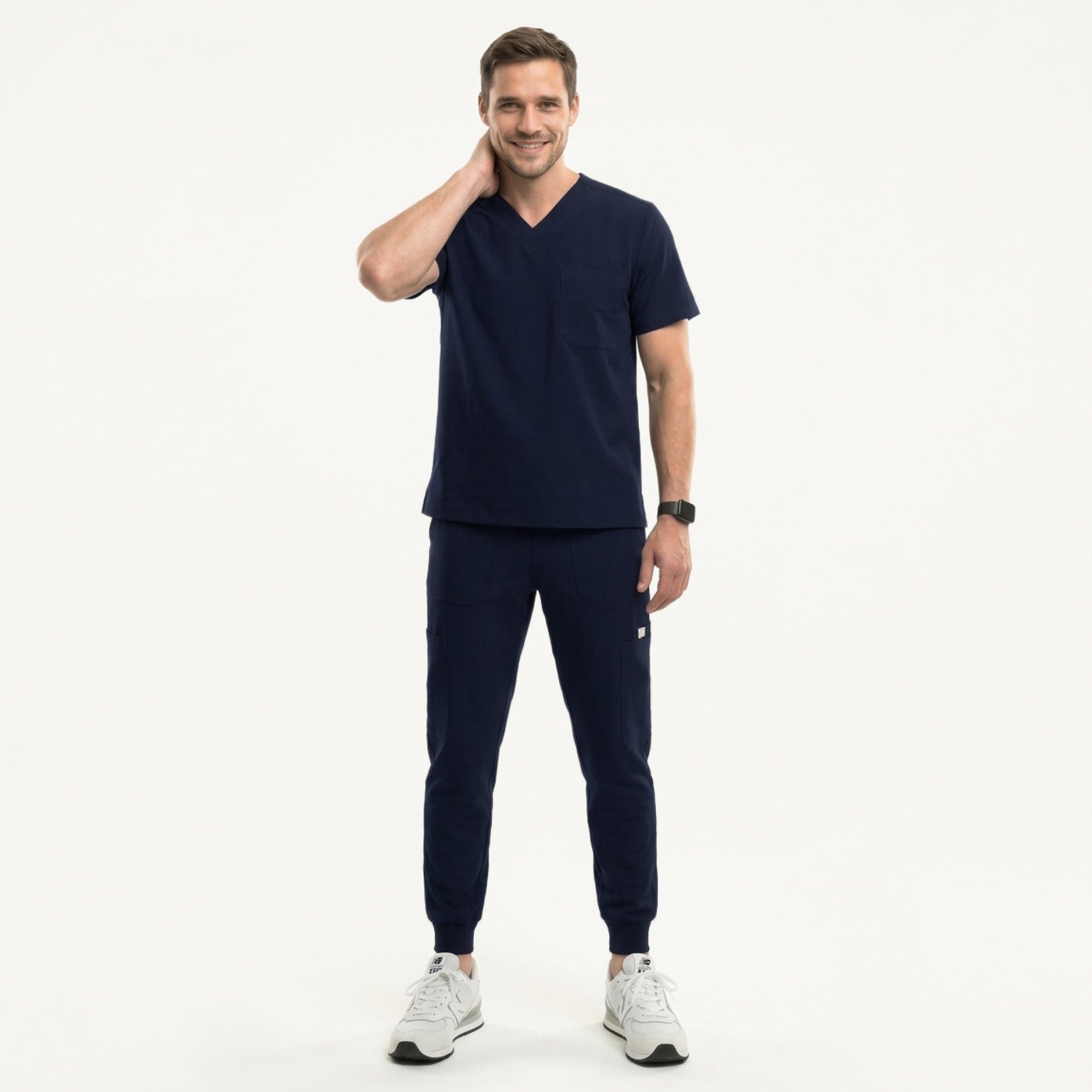 Image of Male healthcare professional wearing a navy V-neck, three-pocket scrub top and matching jogger pants with stethoscope around neck, standing beside a medical cart with supplies,Navy