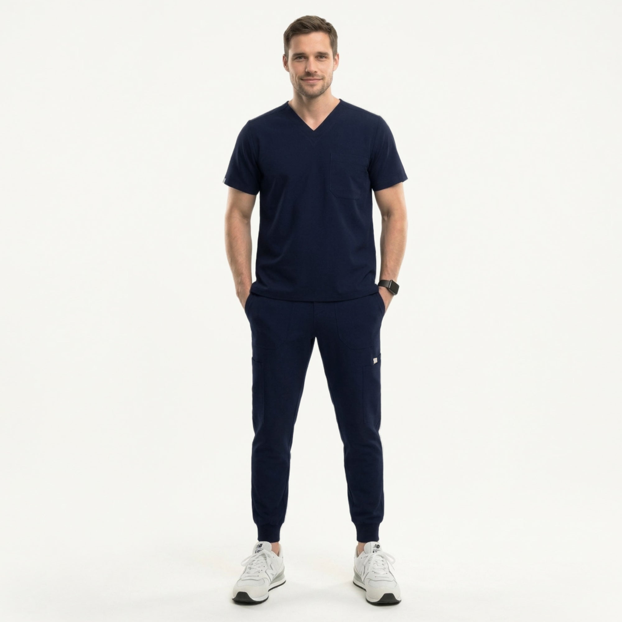 Image of Male healthcare professional wearing a navy V-neck, three-pocket scrub top and matching jogger pants with stethoscope around neck, standing beside a medical cart with supplies,Navy