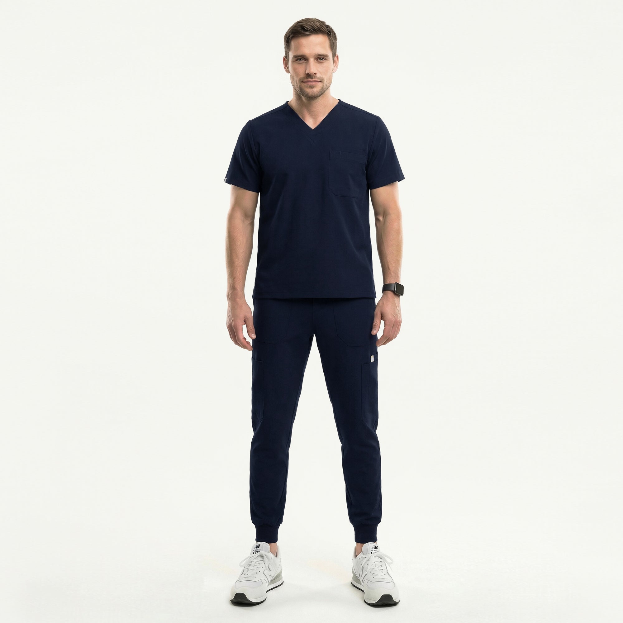 Image of Male healthcare professional wearing a navy V-neck, three-pocket scrub top and matching jogger pants with stethoscope around neck, standing beside a medical cart with supplies,Navy