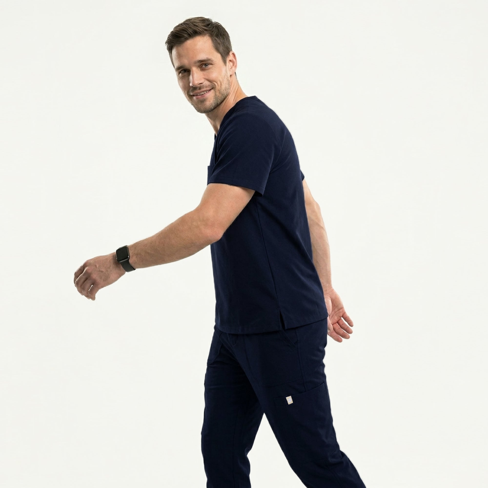 Image of Male healthcare professional in navy V-neck scrub top with stethoscope around neck, arms crossed, looking to the side against a plain background,Navy