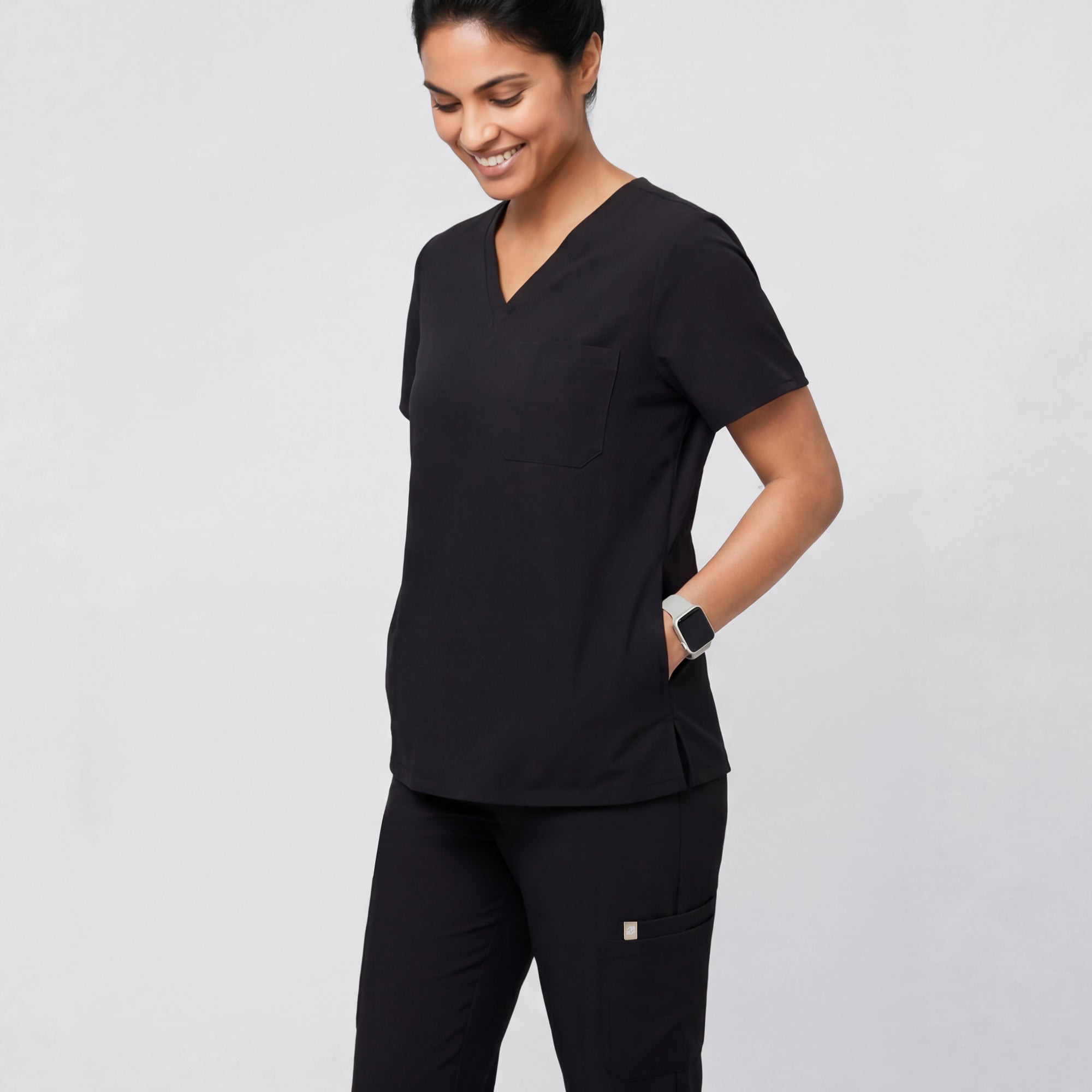 Image of Model wearing the Eco Black 3-Pocket Scrub Top in a relaxed side pose, showing the V-neckline and chest pocket.