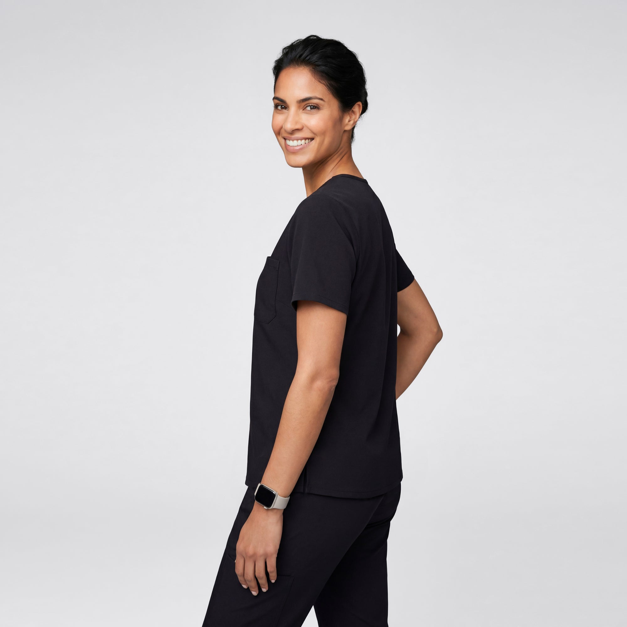 Image of A person shown from the back wearing an Eco Black scrub top with short sleeves, displaying the clean and minimal back design.