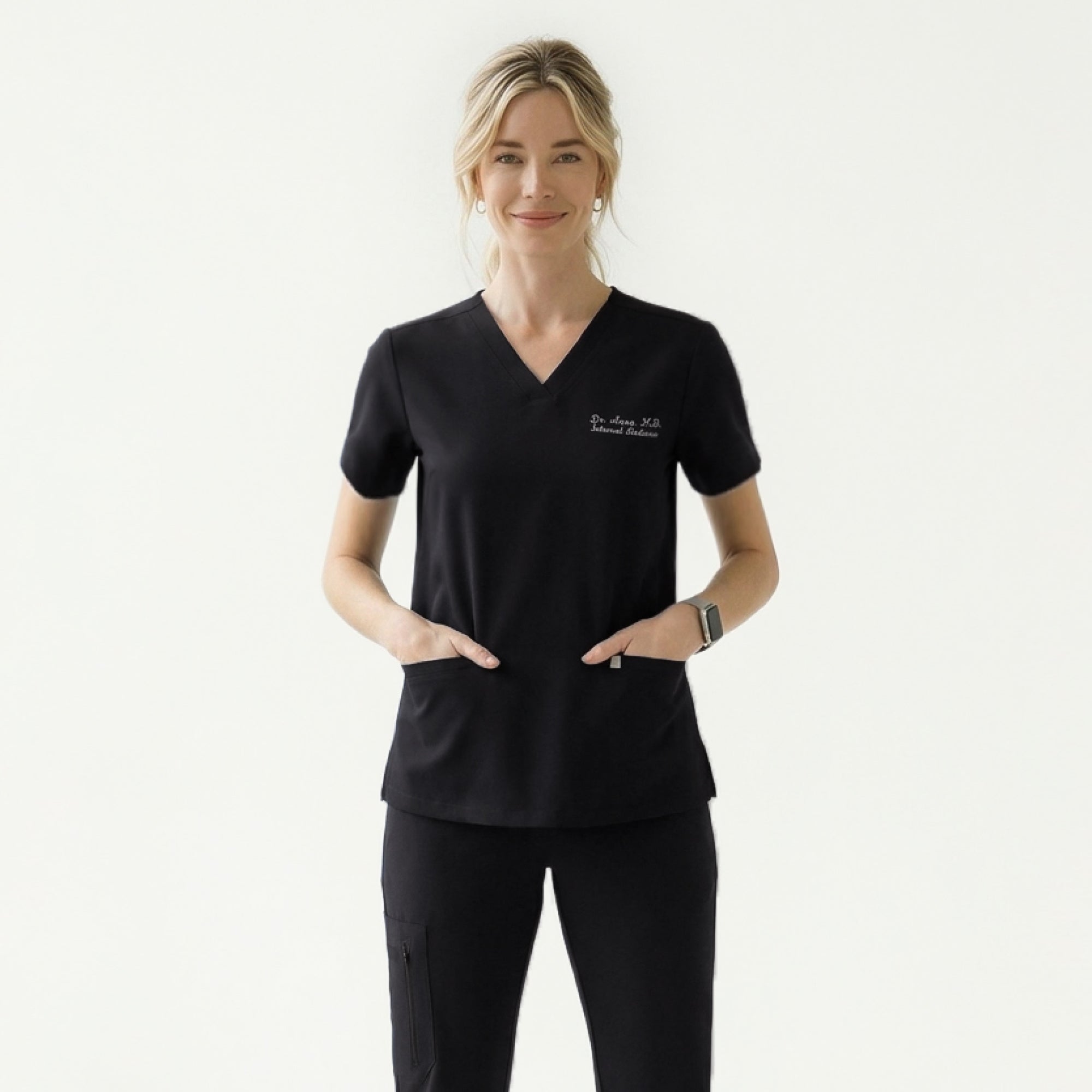 Image of Woman wearing a black V-neck scrub top with embroidered name and double front pockets, paired with matching black scrub pants,Eco Black
