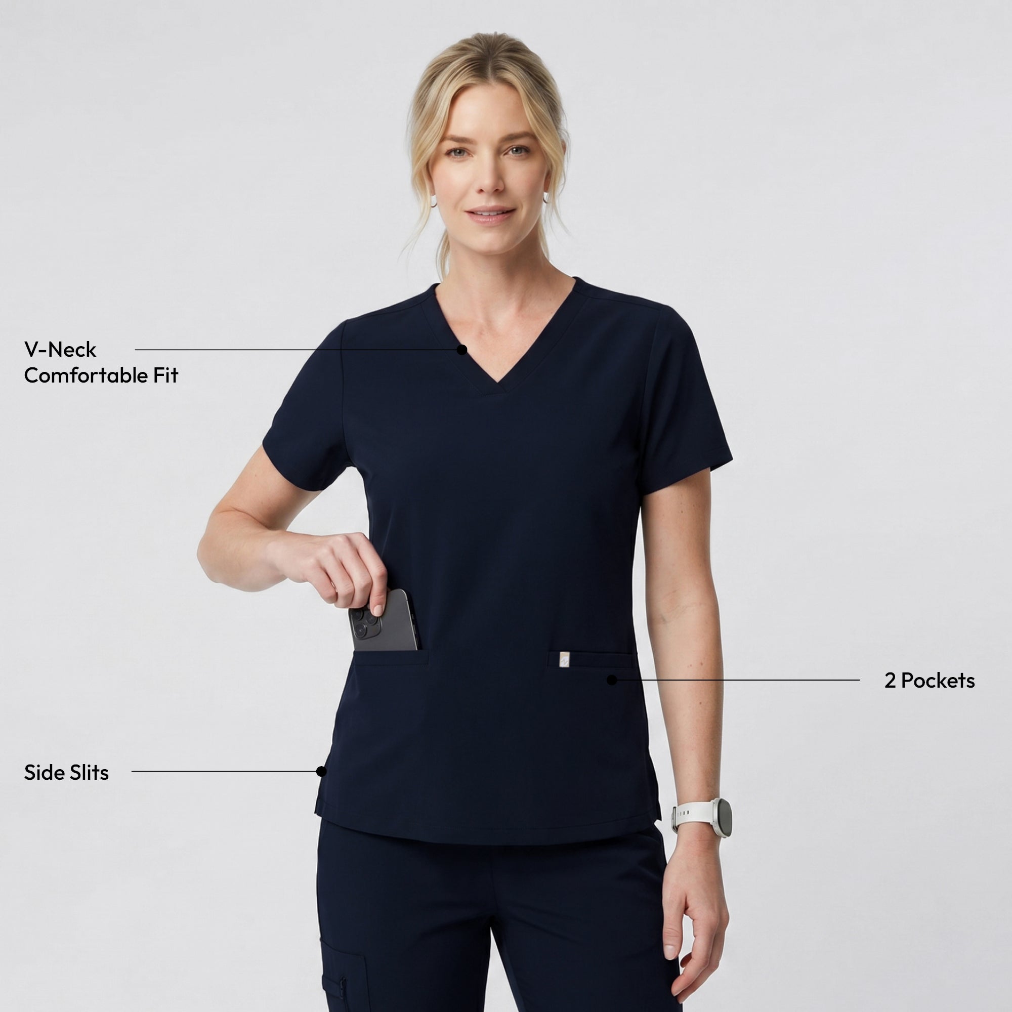 Image of Model dressed in the Women's Eco Navy Double Pocket Scrub Top with pants, smiling with a yellow stethoscope and laptop in hand, upper body shot.