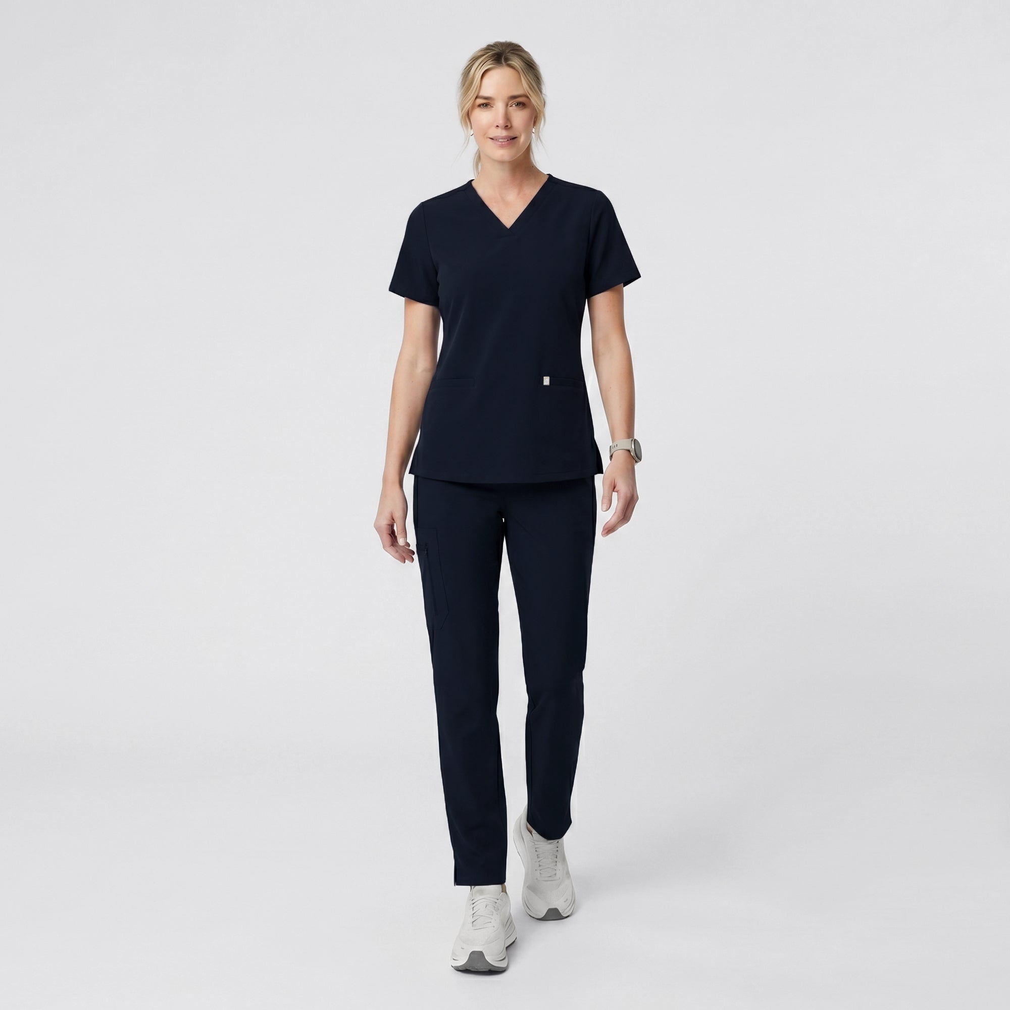 Image of Model wearing the Eco Navy Double Pocket Scrub Top and matching jogger pants, standing with hands in pockets.