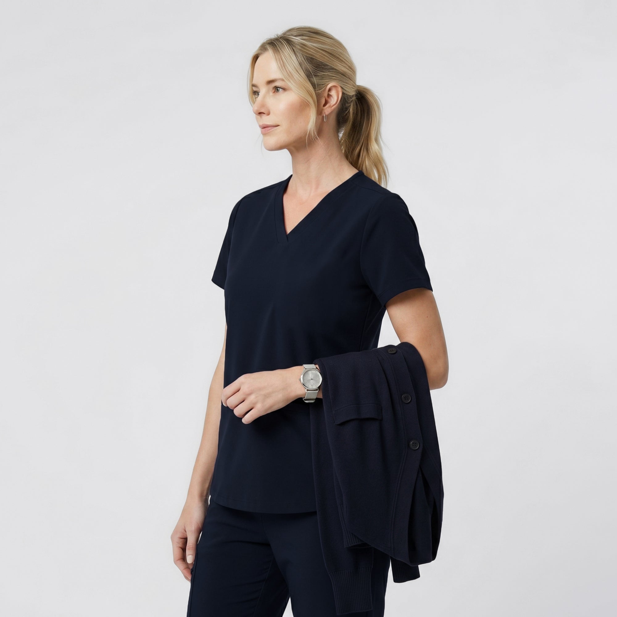 Image of Side view of a model wearing the Eco Navy Double Pocket Scrub Top with hands in pockets.