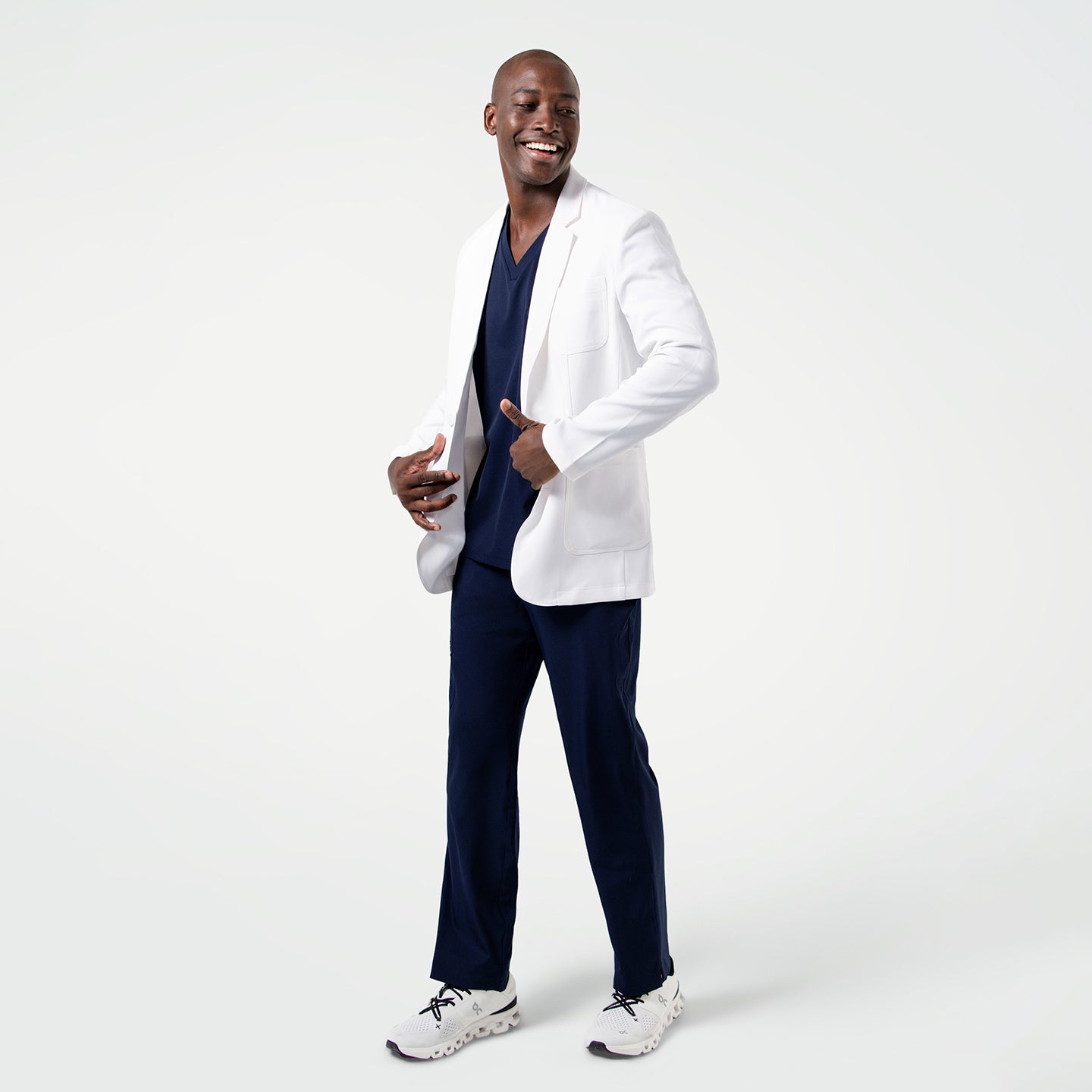 Image of Male model in the Men's LCM-100 Lab Coat in White over medical scrubs, full body view, smiling while standing with hands near the coat pockets