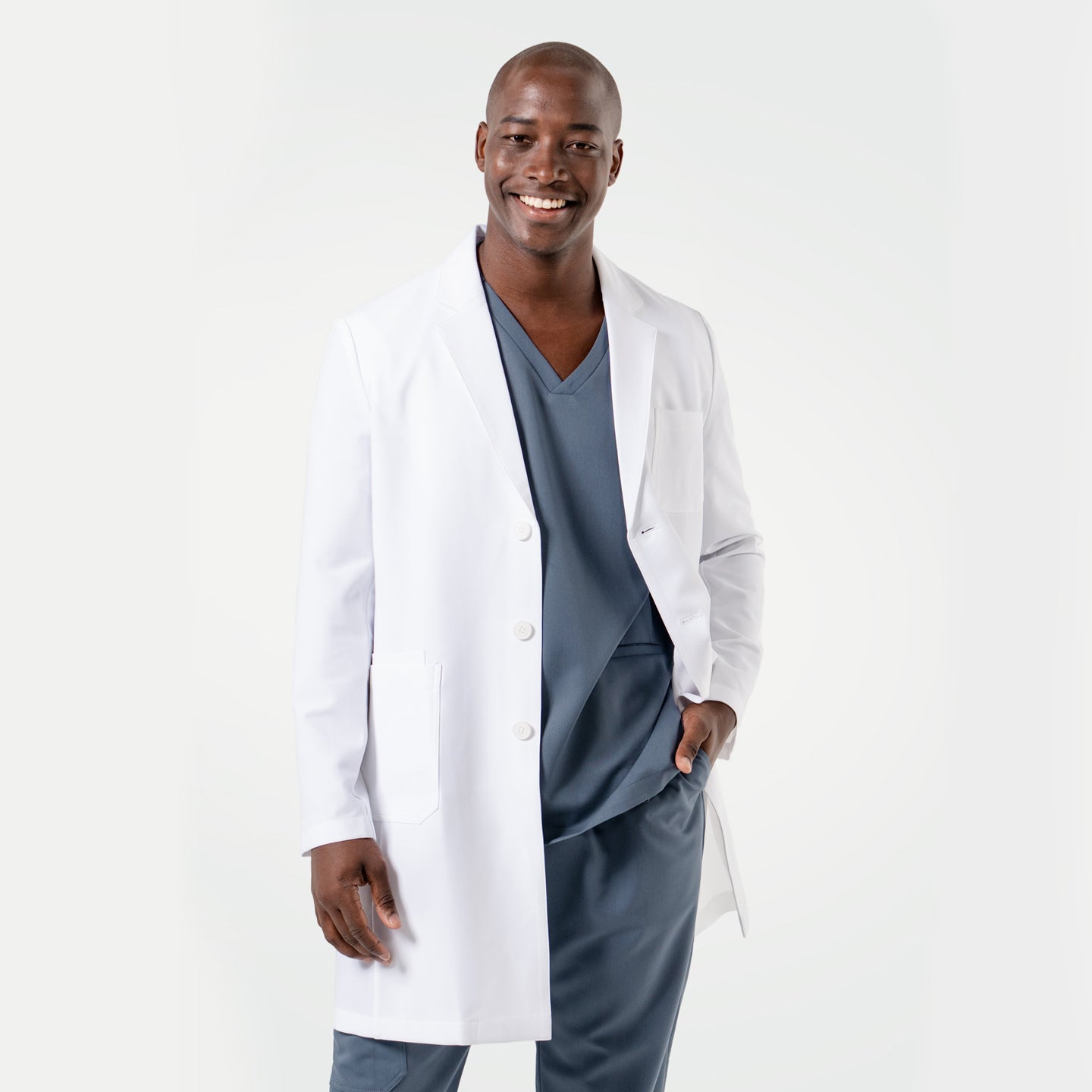 Image of Smiling in the Men's LCM-101 Lab Coat in White over medical scrubs, one hand in the pocket, full body view