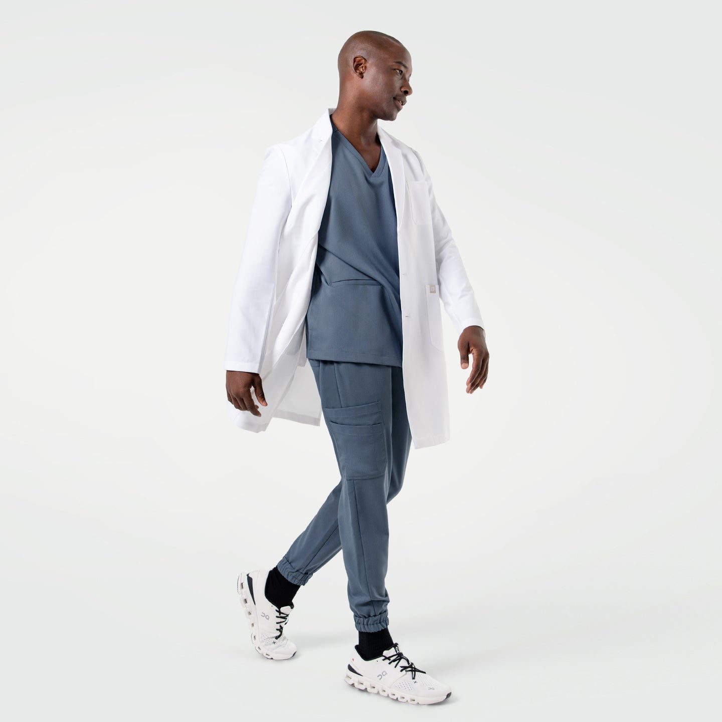 Image of Walking in the Men's LCM-101 Lab Coat in White over medical scrubs, side view, full body shot