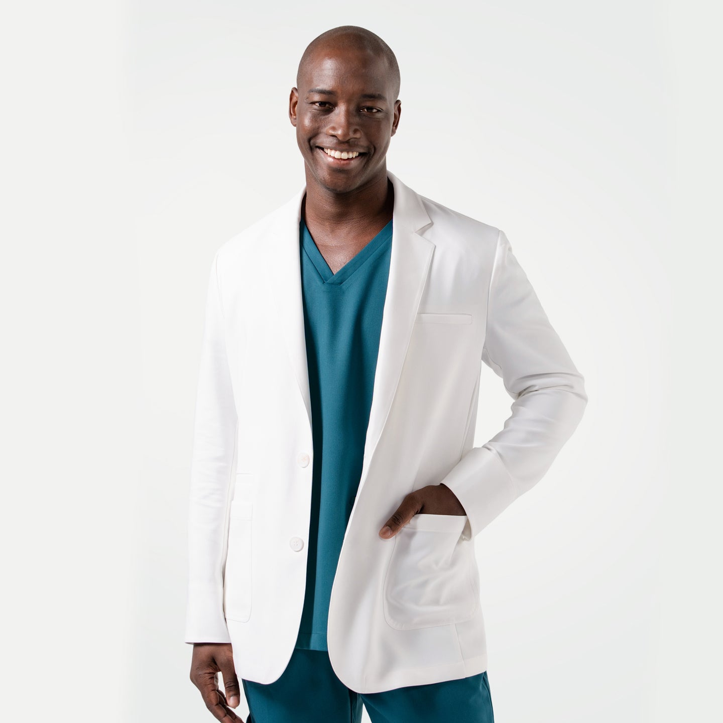 Wearing the Men's LCM-102 Lab Coat in White over medical scrubs, smiling confidently with one hand in the pocket, upper body view