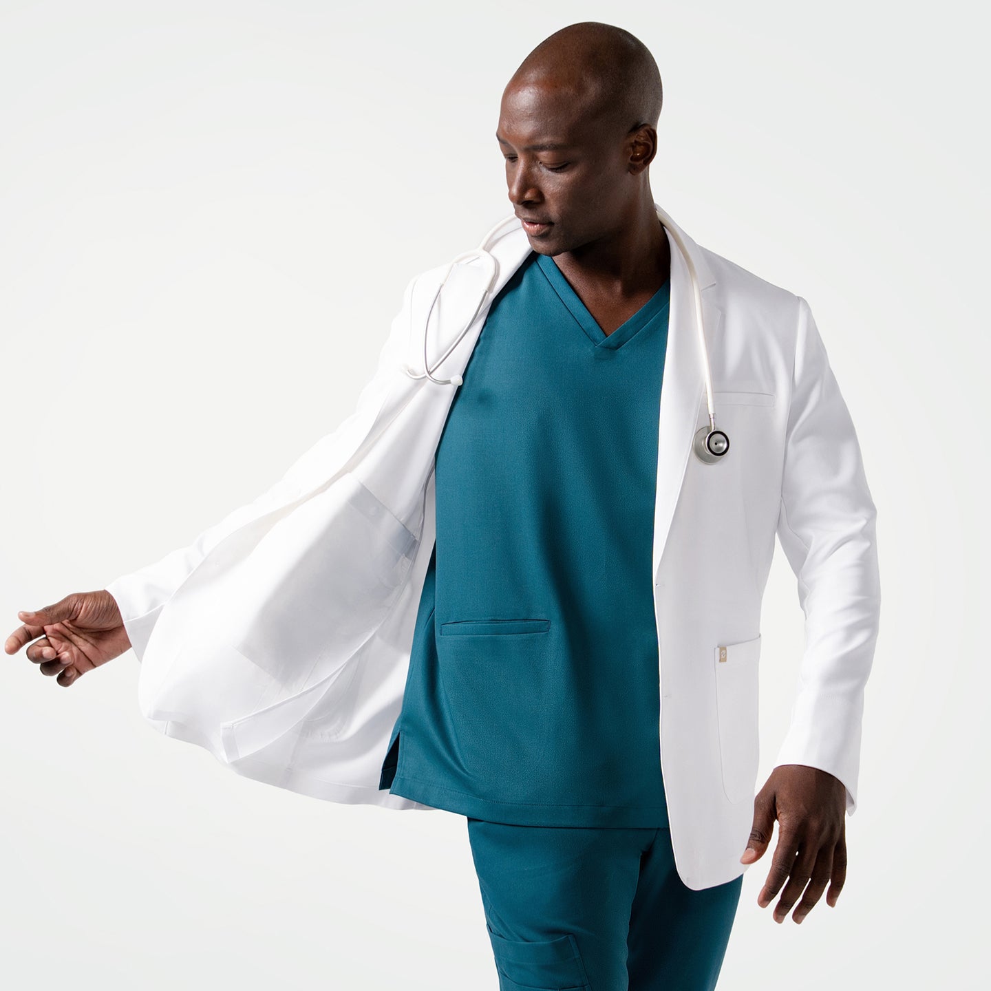 Image of Wearing the Men's LCM-102 Lab Coat in White over medical scrubs, looking down while holding one side of the coat with a stethoscope around the neck