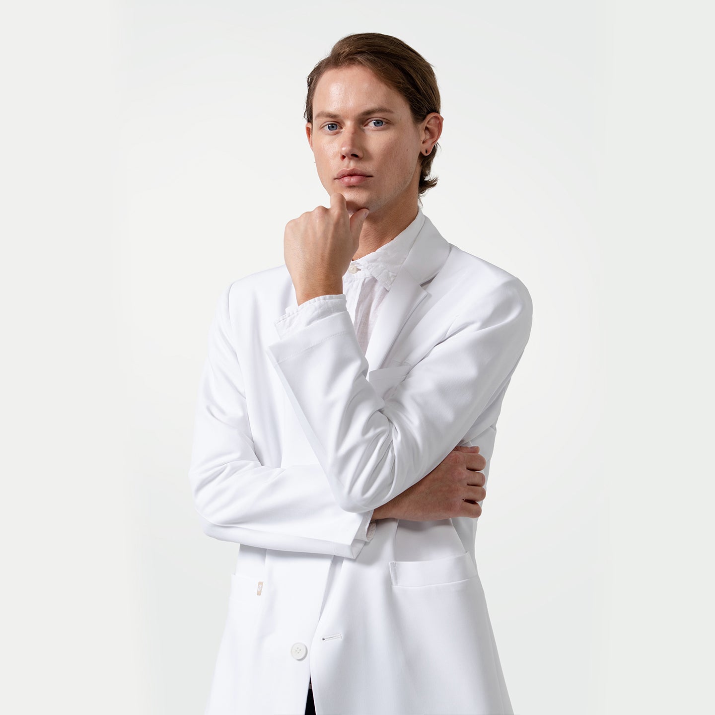 Image of Male model wearing a white Lcm-103 lab coat over a white shirt, standing with one hand on chin and the other arm folded.