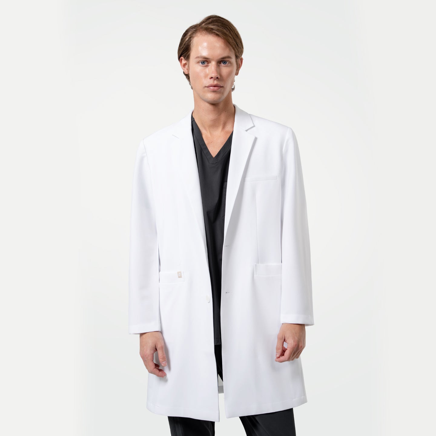 Image of Lcm-103 men’s white lab coat front view, worn over black scrubs, featuring modern tailored fit and clean professional design.