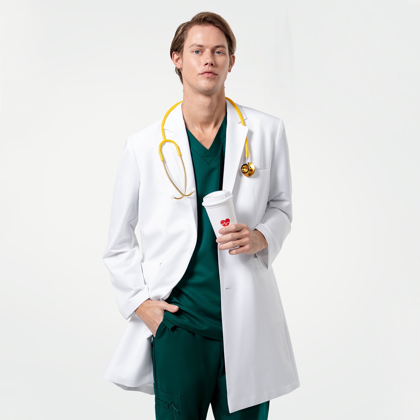 Image of Holding a coffee cup, wearing the Men's LCM-103 Lab Coat in White over medical scrubs with a yellow stethoscope around the neck, one hand in the pocket