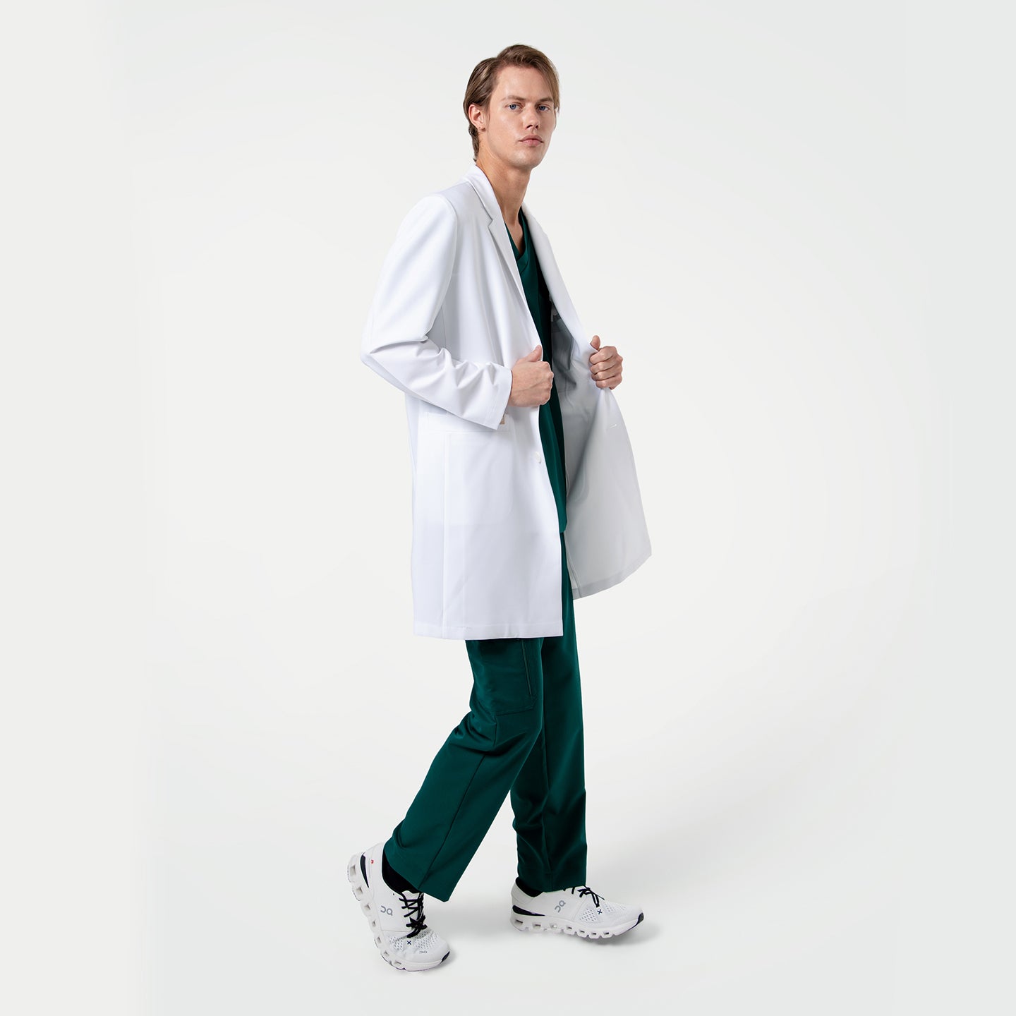 Image of Person wearing a white lab coat over pine green scrubs on a white background