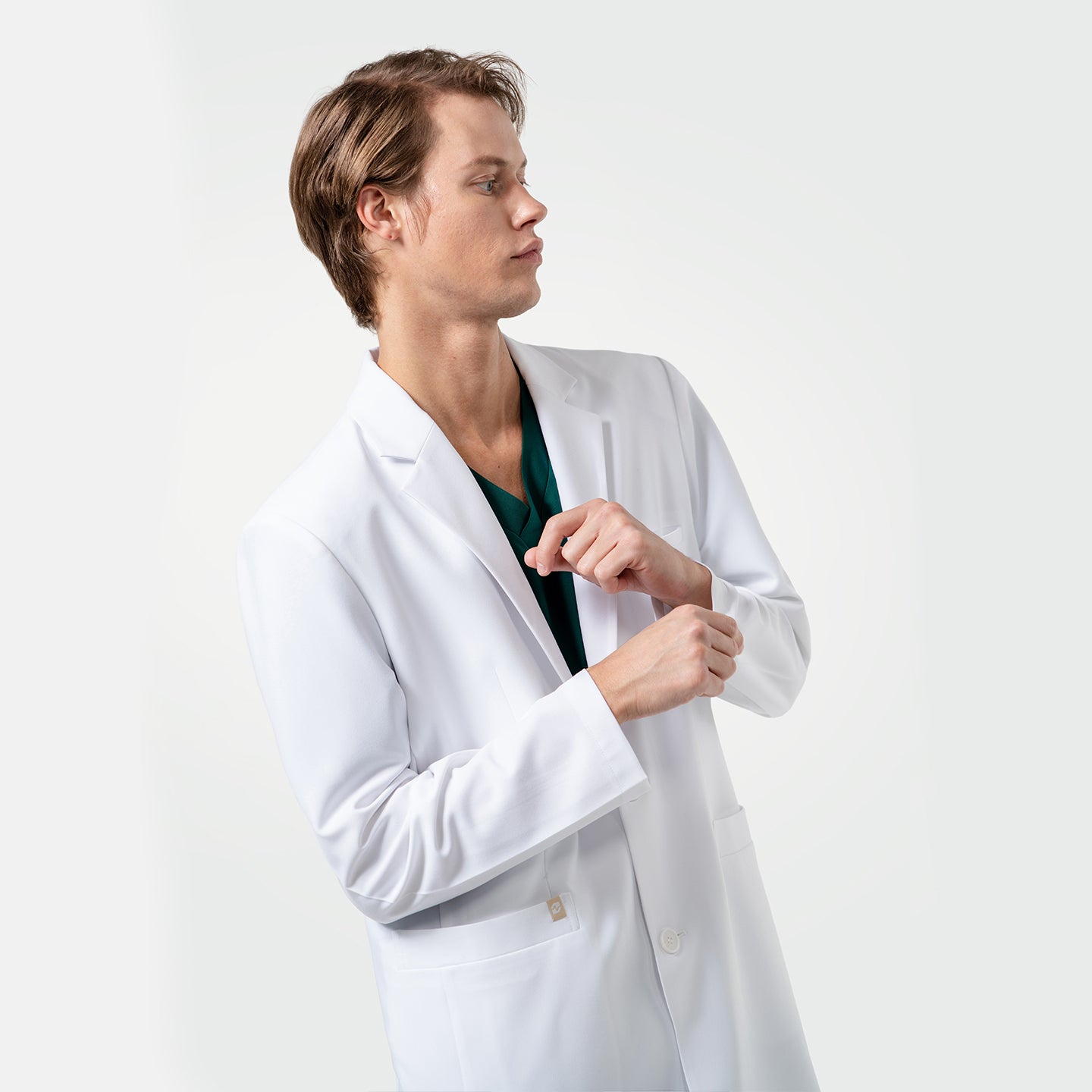 Image of With a focused expression, a male healthcare professional in a white coat over green scrubs adjusts his sleeve