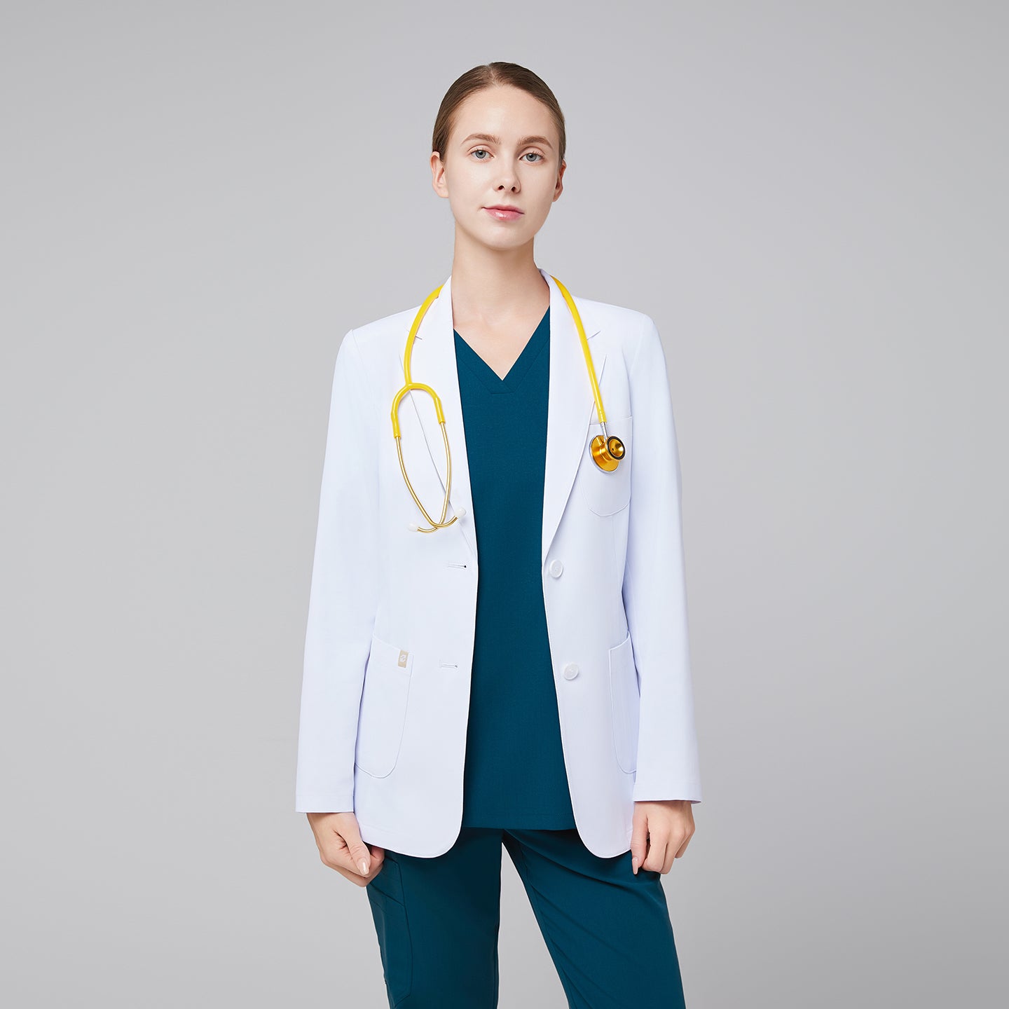 Image of Model facing forward wearing a white short lab coat with chest and side pockets, and blue scrub top and bottom under, with yellow stethoscope around her neck,White