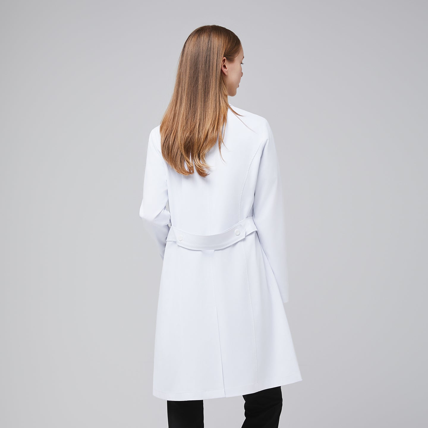 Image of Model facing back, with a white long lab coat and black scrub top, black scrub pants, and black sneakers,White