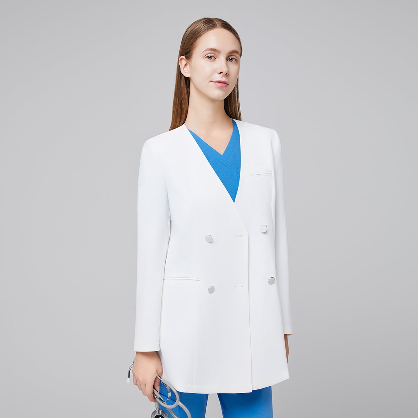 Image of Front view of a woman wearing a white double-breasted long lab coat over a blue scrub top, holding a stethoscope,White