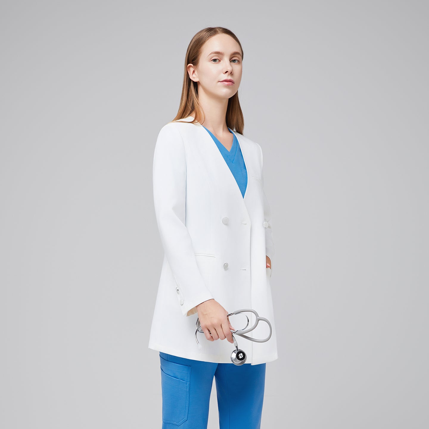 Image of Side view of a woman in a white double-breasted lab coat with buttoned cuffs, layered over a blue scrub outfit,White