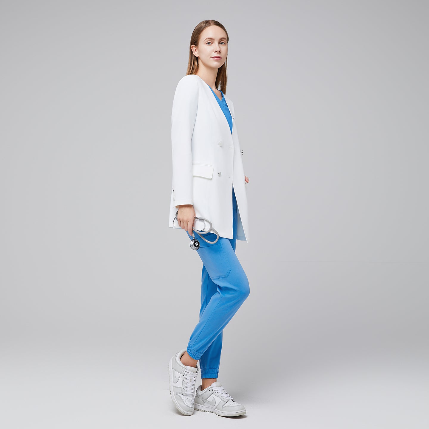 Image of Full-body shot of a woman in a white long lab coat with silver buttons, paired with blue scrub pants and white sneakers,White
