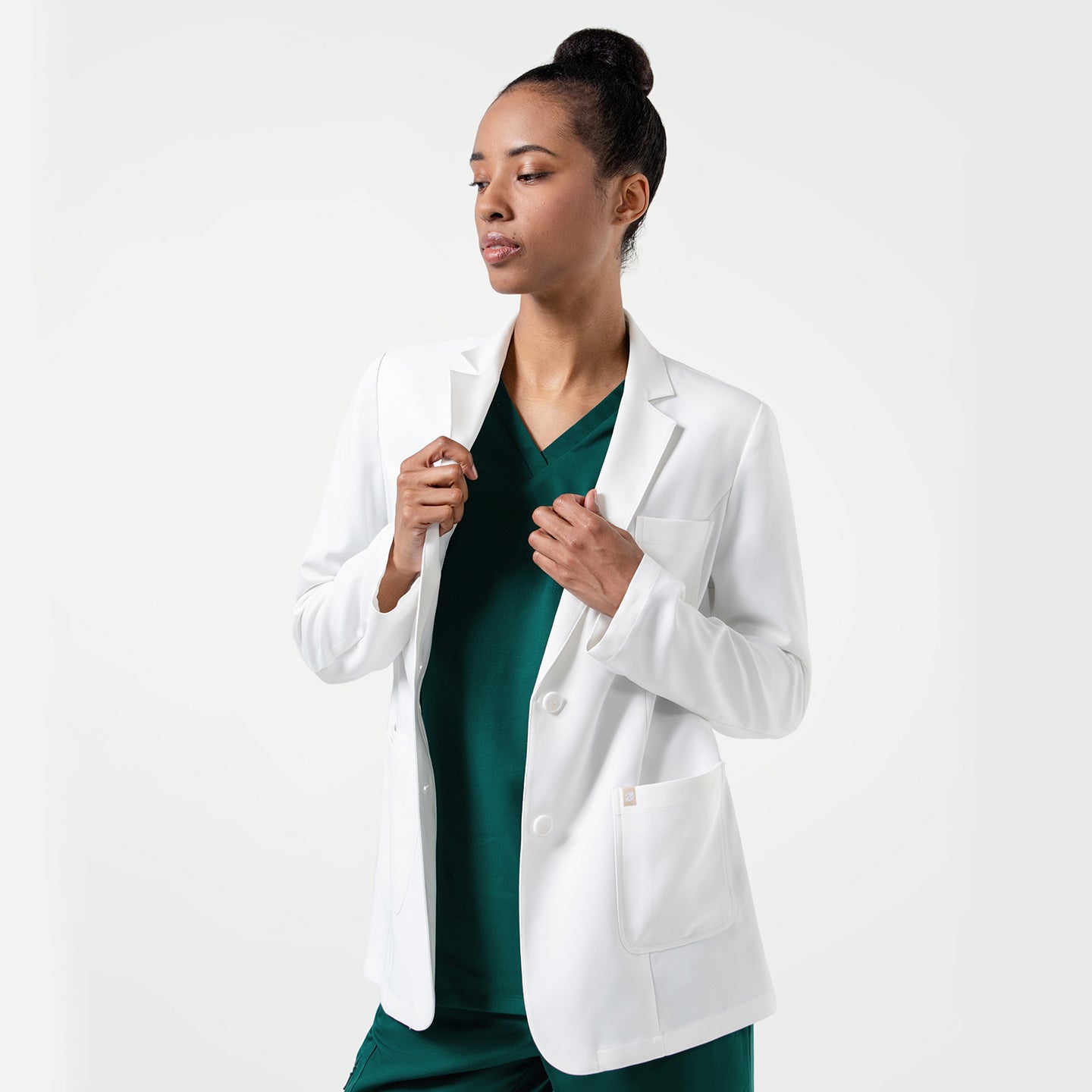 Image of Woman holding the Women's LCW-101 Lab Coat in White over pine green scrubs, looking slightly to the side, upper body view