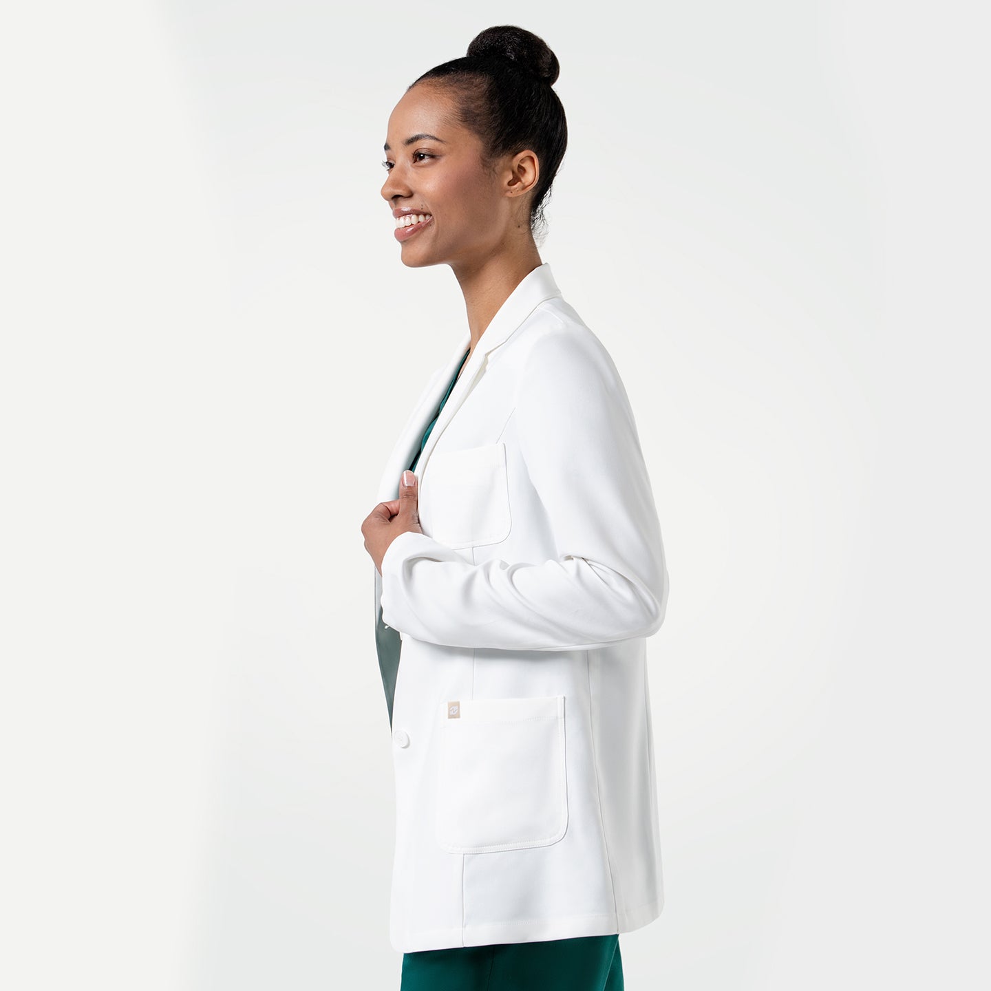 Image of Upper body shot of the model wearing the Women's LCW-101 Lab Coat over pine green scrubs, smiling while looking to the side