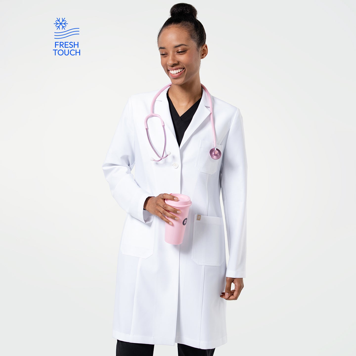 Image of Model in the Women's LCW-102 Lab Coat in White over medical scrubs, smiling while looking slightly to the side with a pink stethoscope around her neck and holding a pink tumbler