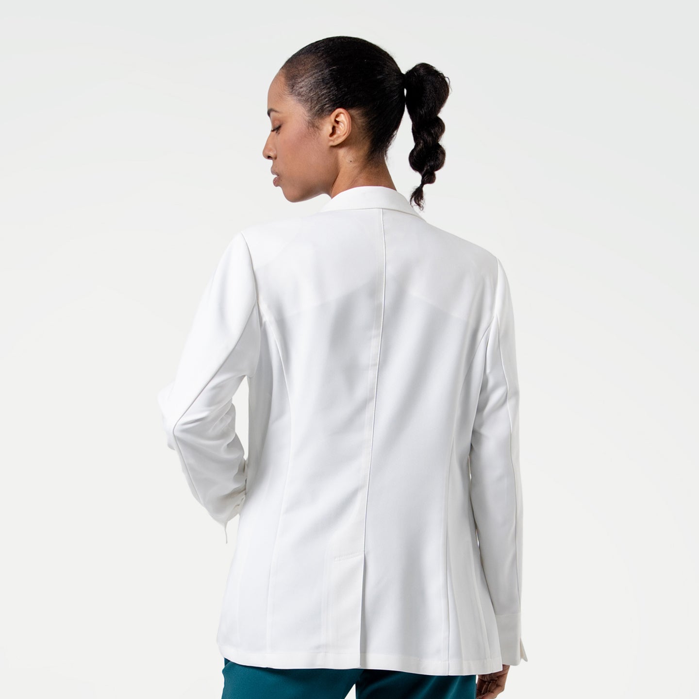 Image of From behind, the model in the Women's LCW-04 Lab Coat in White over medical scrubs turns slightly to the side, upper body view
