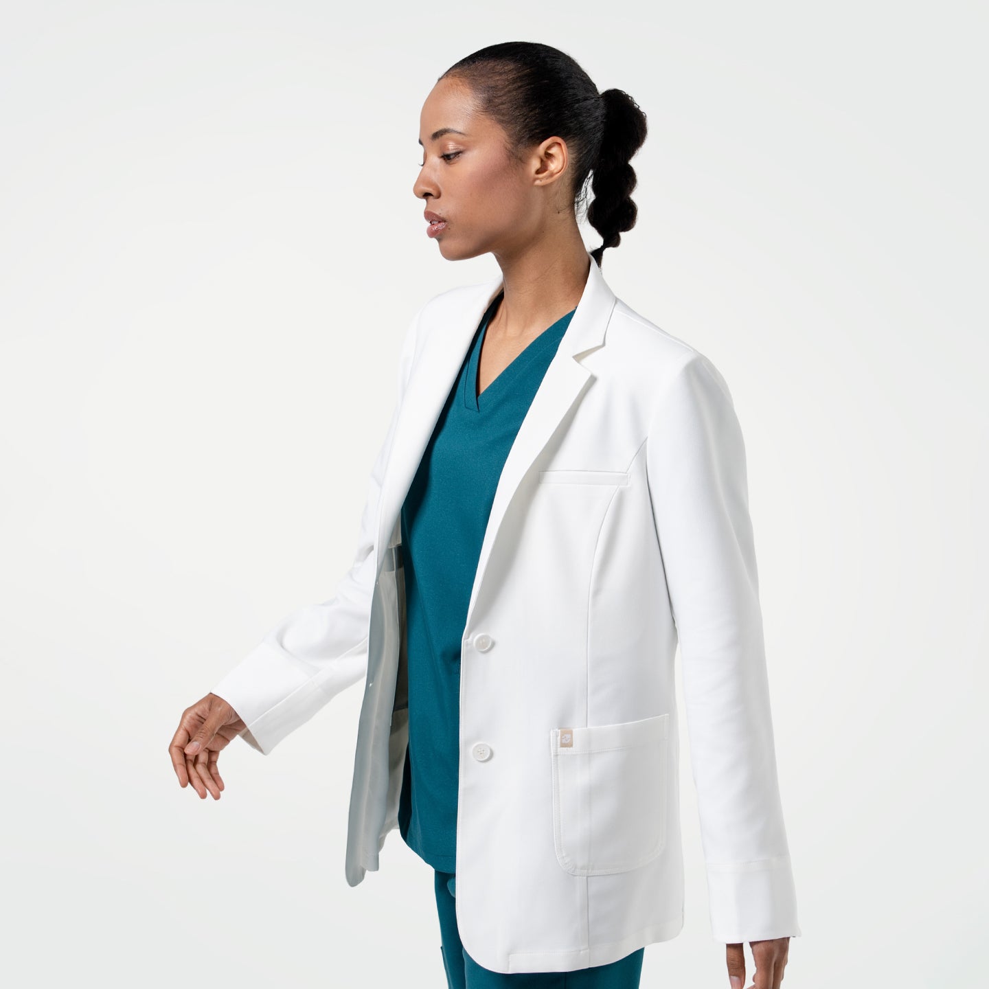 Image of Mid-step, the model in the Women's LCW-04 Lab Coat in White over medical scrubs is captured from the side, upper body view only