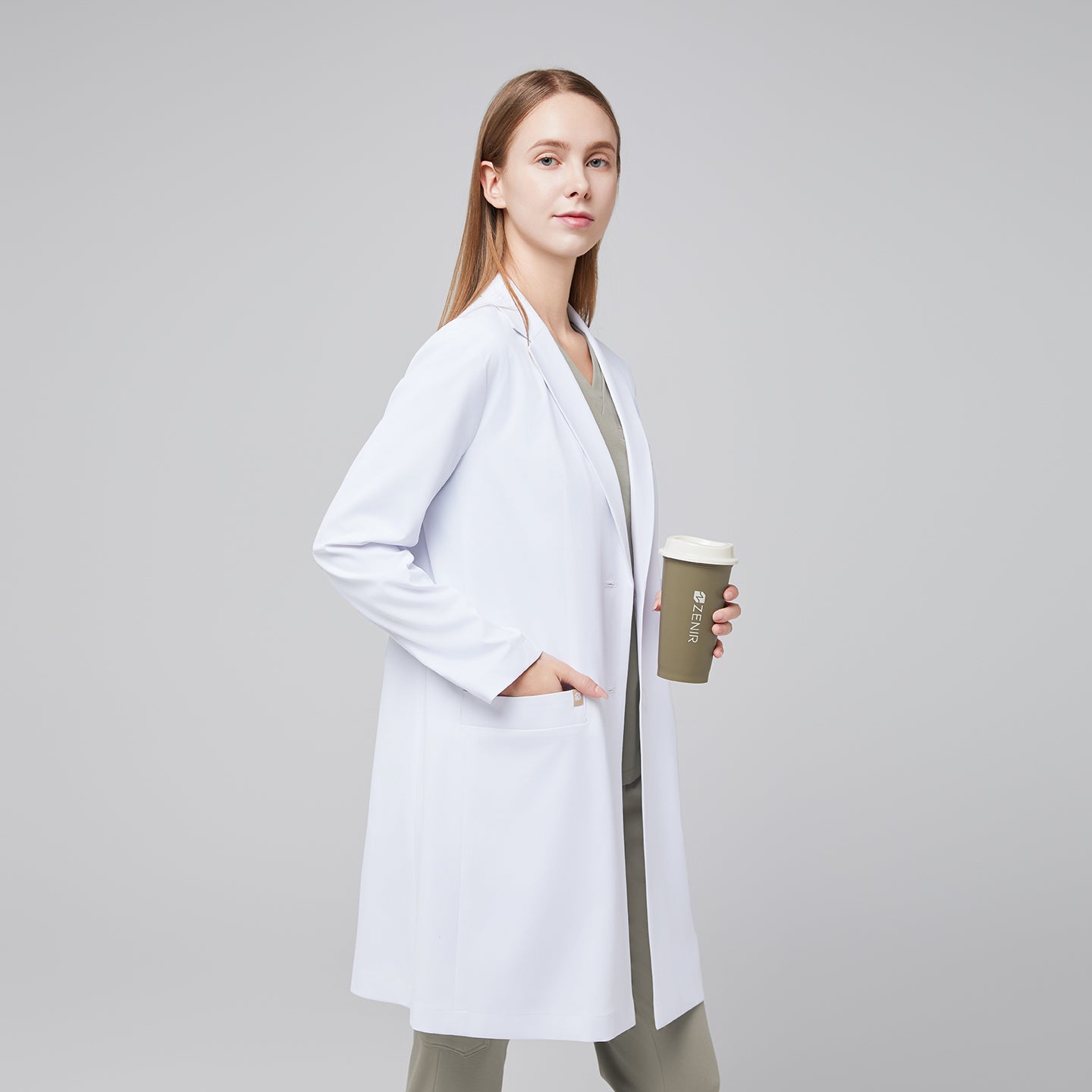 Image of LCW-204 A clean, tailored white lab coat featuring a modern notch collar, two front pockets, and a streamlined fit, worn over light sage scrubs for a polished professional look.