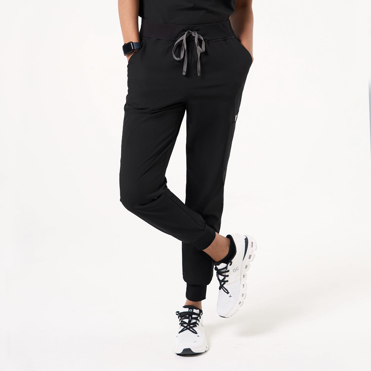 Hands are in both pockets while one leg crosses over the other, wearing Eco Black jogger scrub pants.