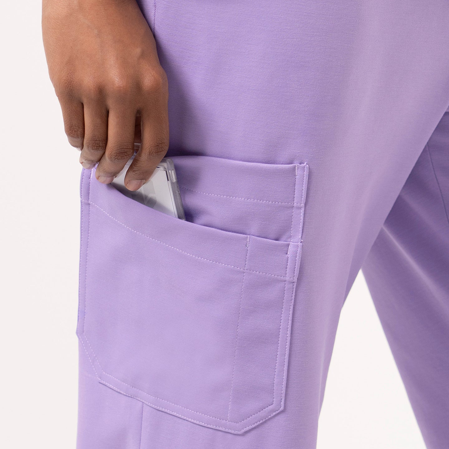 Image of Close-up of Straight Split Hem Scrub Pants in Lavender, showing a hand placing a phone into the side pocket.