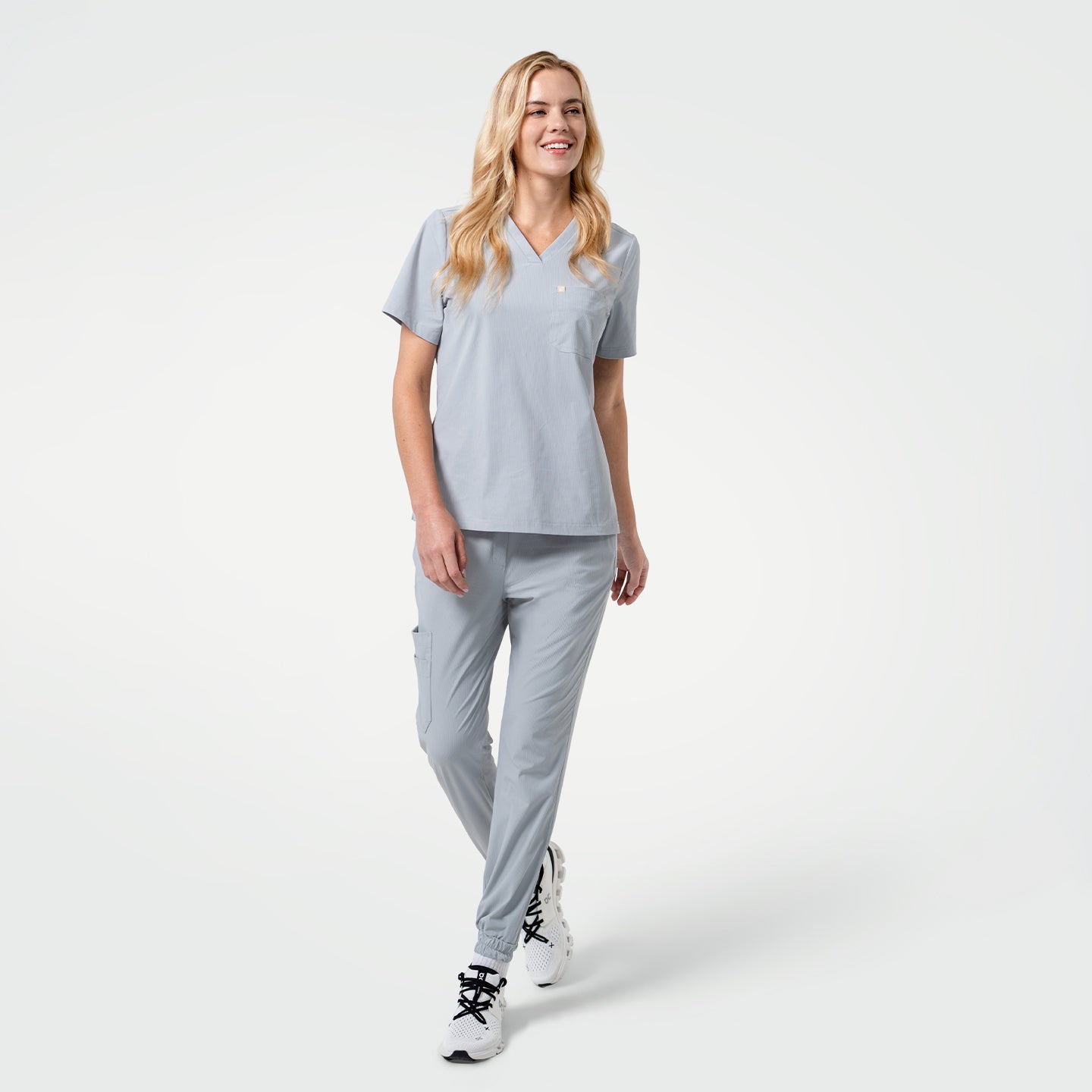 Image of A woman walking while wearing StretchFit Jogger Scrub Pants in Cool Gray with a matching V-neck scrub top and white sneakers.