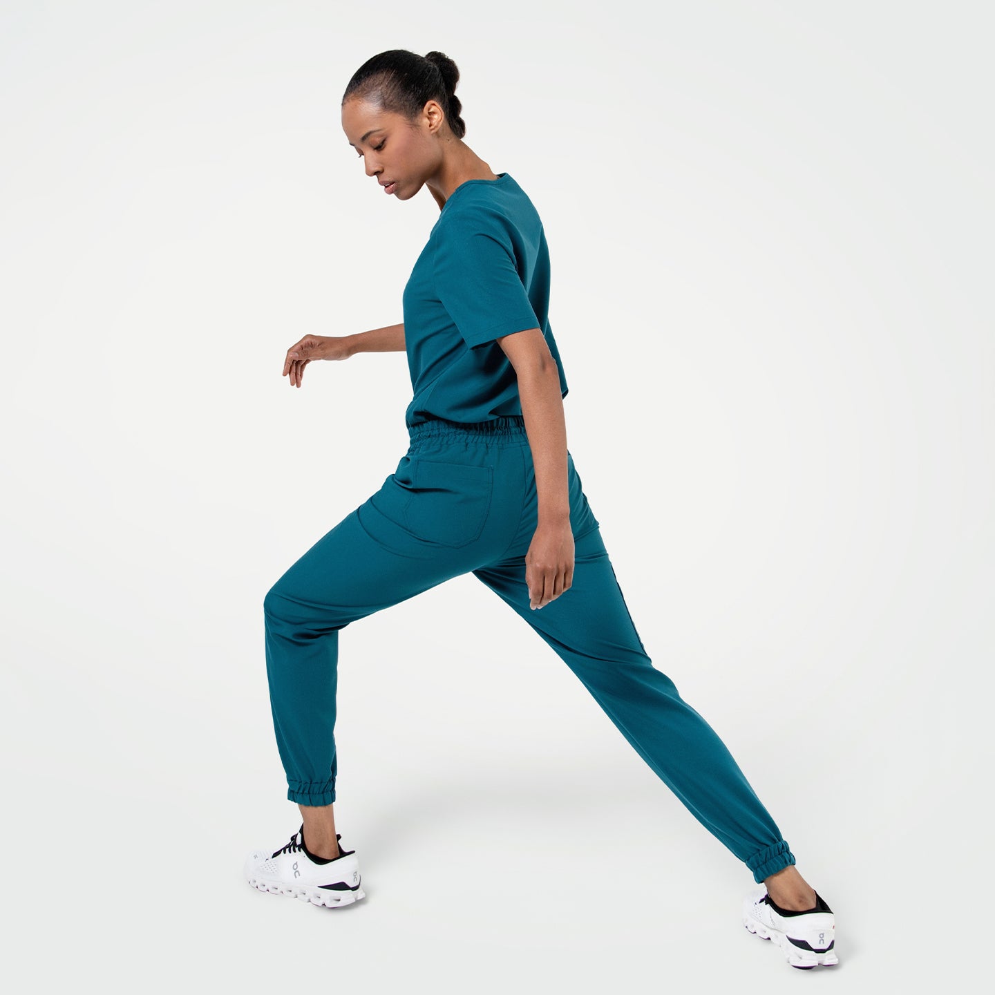 Image of Person wearing StretchFit Jogger Scrub Pants in Ocean Teal, performing a side lunge with one leg bent and the other extended straight.