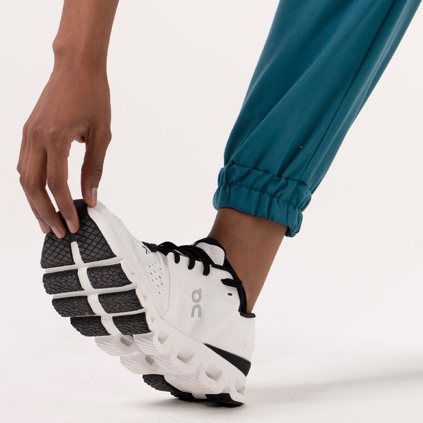 Close-up of a person wearing StretchFit Jogger Scrub Pants in Ocean Teal, bending down to touch their shoe near the ankle cuff.