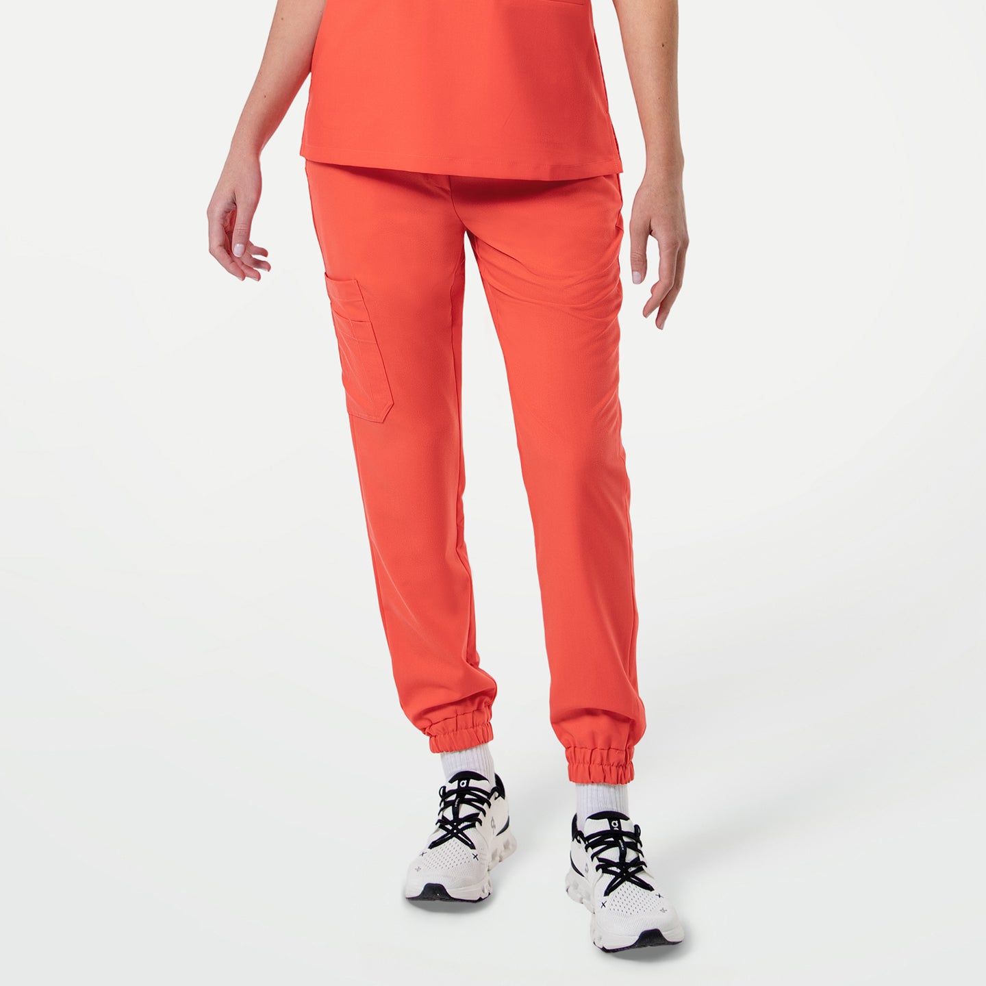 Image of Model wearing StretchFit Jogger Scrub Pants in Tiger Orange, standing with arms relaxed at the sides, showing front view with flap pocket detail on the thigh and elastic cuffs at the ankles.