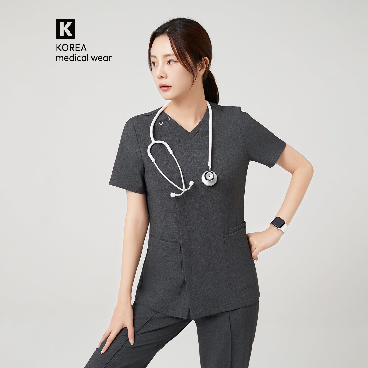 The Charcoal Gray OS-228 features the model in a confident side pose with one hand on her waist, highlighting the scrub’s structured silhouette and professional design.