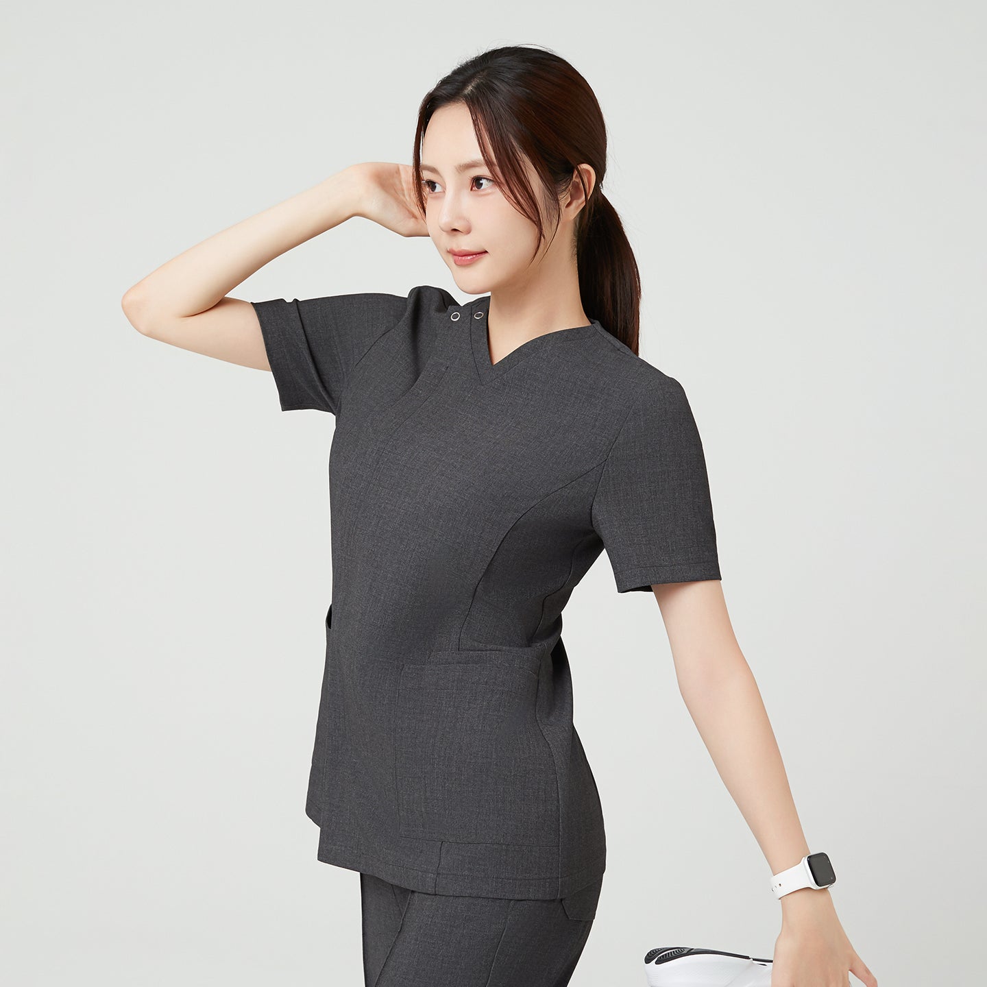 Charcoal Gray OS-228 poses gracefully with one arm raised, showcasing the scrub’s flattering fit and flexible structure.
