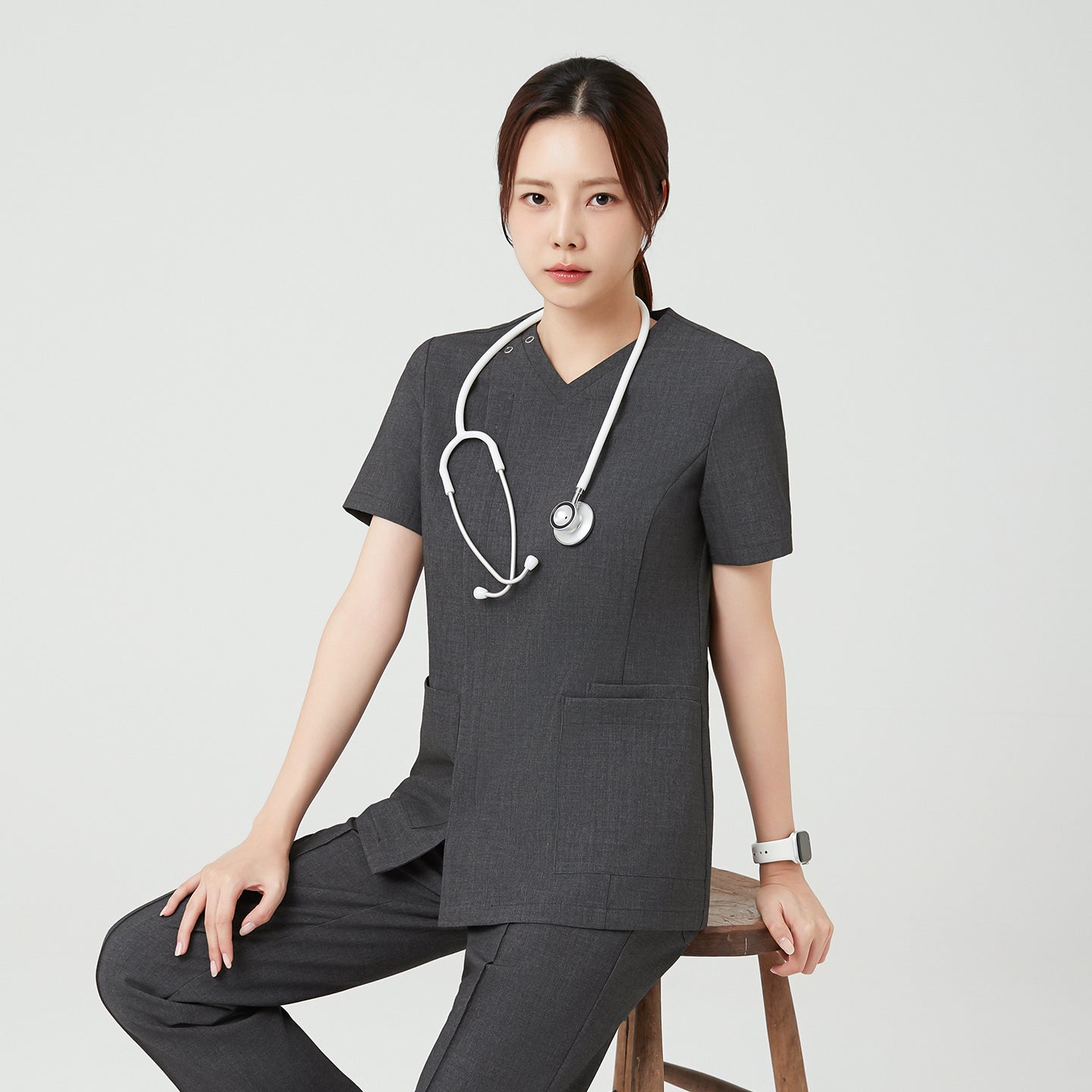Seated with a composed expression, the model in Charcoal Gray OS-228 highlights the uniform’s structured silhouette and calm, professional appeal.