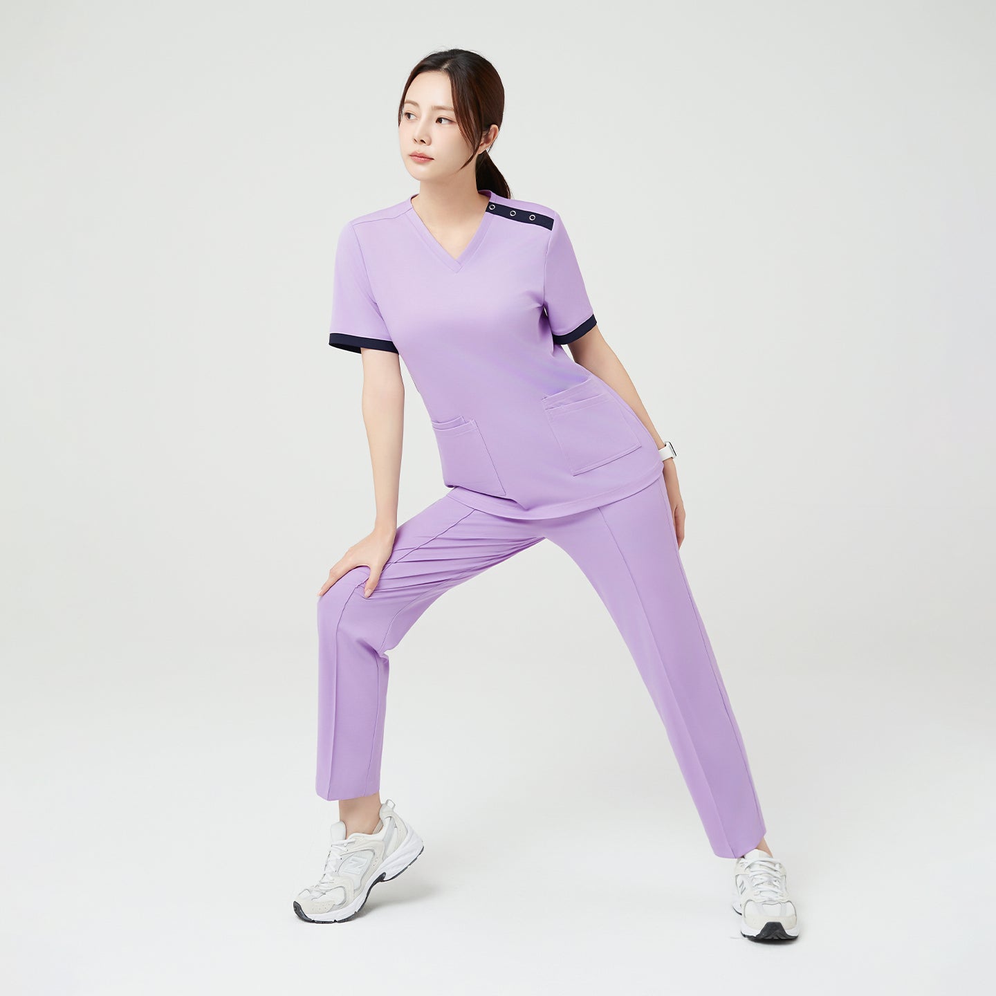 Image of The model strikes a light stretch pose in the Lavender OS-230 scrub set, emphasizing the outfit’s flexibility and ease of movement — perfect for active, all-day comfort.