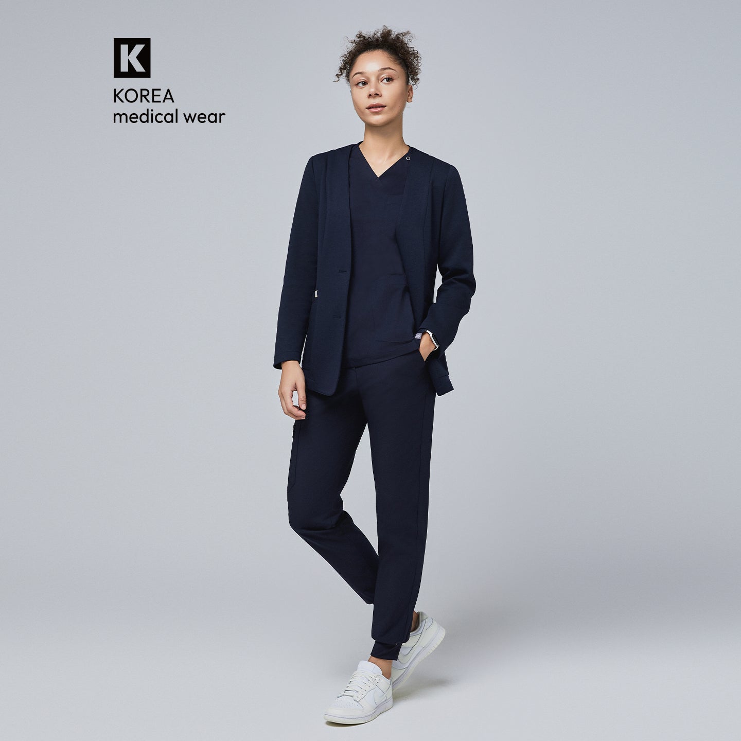 Image of Woman wearing a navy comfort cardigan over a matching V-neck scrub top and jogger scrub pants, paired with white sneakers for a professional yet relaxed look,Navy